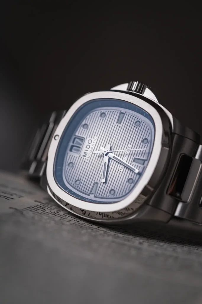 Close-up of a blue-faced stainless steel wristwatch at an angle, showing the ribbed dial and crown.